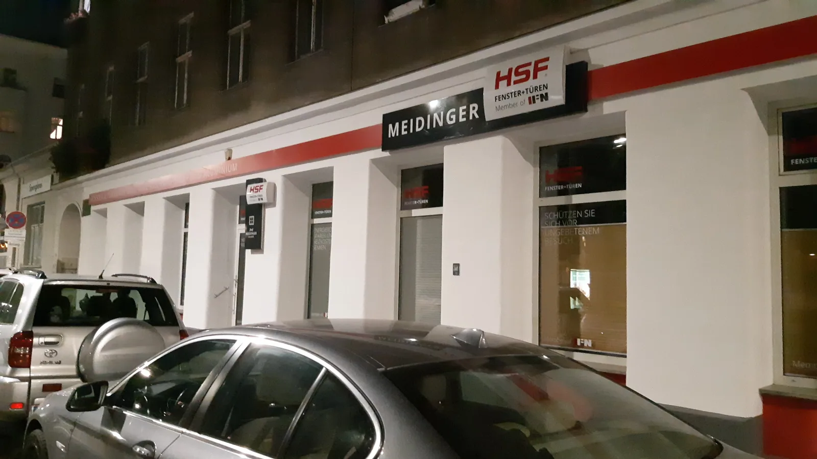 Ladenfront von Meidinger am Abend in Schrägansicht, Schild MEIDINGER über den Schaufenstern