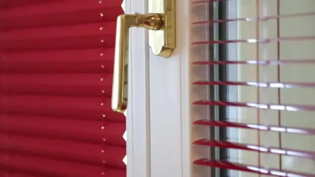 Fenstergriff aus Messing vor einem roten Plissee und einer Jalousie im Schauraum